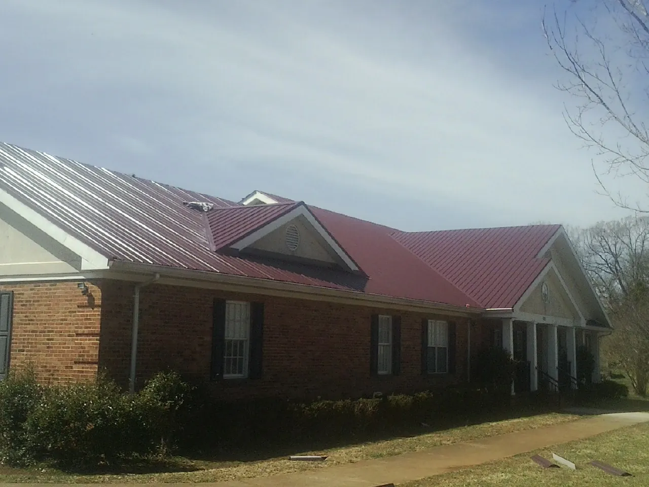 Red metal roof with gabled entries on a long brick building, from a Hail Damage Roof Repair job in Thurmont