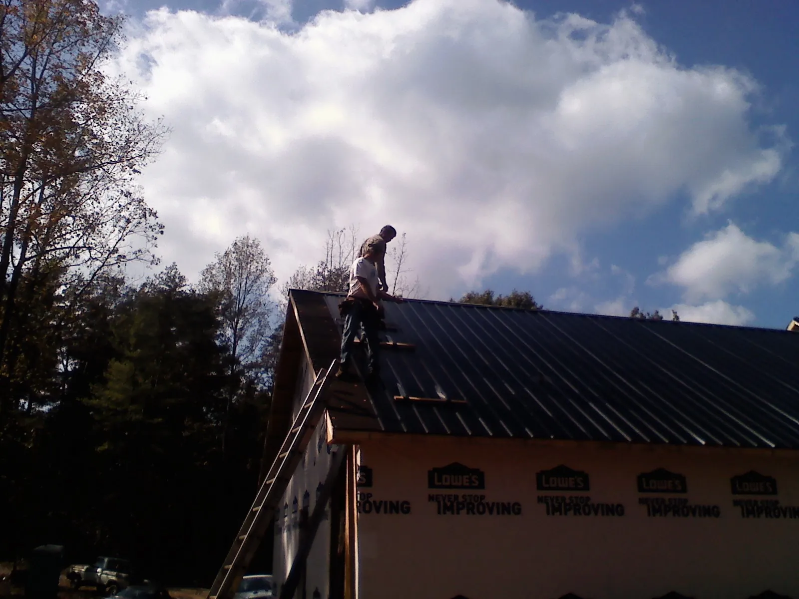 Roofer fastening dark metal panels high against a cloudy sky, from a Roof Inspection job in Thurmont