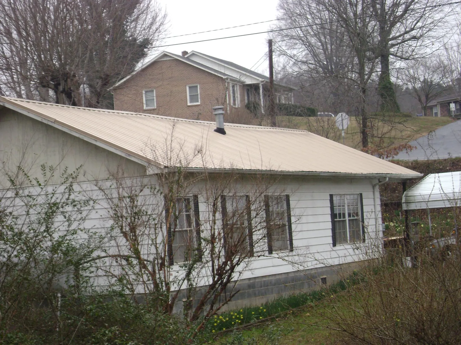 Tan metal roof on a white sided house set into a hillside — Commercial Roofing by Roofing Brothers in Thurmont